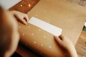 as mãos da menina embrulham a caixa de papelão em papel kraft na mesa de madeira. foto