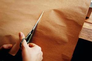 mãos cortam a folha de papel artesanal com uma tesoura. foto