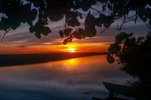 lindo pôr do sol às rio com árvores e uma barco foto