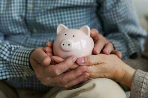 salvando dinheiro investimento para futuro. Senior adulto maduro casal mãos segurando porquinho banco com dinheiro moeda. velho homem mulher contando salvando dinheiro planejamento aposentadoria orçamento. investimento bancário conceito. foto