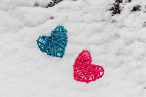 dois corações de vime rosa e azul em um tronco de árvore coberto de neve. o conceito de dia dos namorados foto