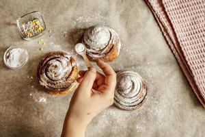 mão de mulher polvilha açúcar de confeiteiro em pães de canela recém-assados foto