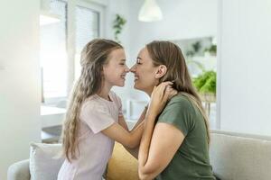 fechar acima do doce bonita filha abraço com dela jovem mãe. adorável mãe abraçando dela fofa filha em a sofá às lar. foto