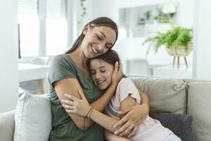 retrato do feliz jovem mãe jogar abraço e abraçar mostrar amor fofa pequeno pré-escolar filha relaxante dentro vivo sala, sorridente mãe e pequeno menina criança descansar apreciar família final de semana às casa juntos foto