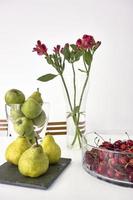 maçãs e peras frescas perto de um vaso de cerejas na mesa foto