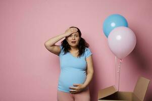 emocional surpreso mulher sentindo-me choque às gênero festa, esperando gêmeos Garoto e garota, segurando cabeça e tocante barriga foto