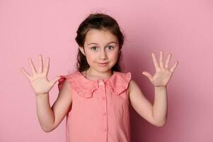 estúdio retrato do coquete doce bebê garota, adorável criança mostrando mãos Palmeiras para a Câmera, isolado Rosa fundo foto