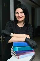 retrato do a atraente confiante com experiência mulher médico dentro uma Preto médico uniforme, segurando educacional livros foto