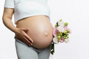 fechar-se grávida barriga do gravídico mulher com uma ramalhete do flores, isoladas em branco estúdio fundo. saudável gravidez foto