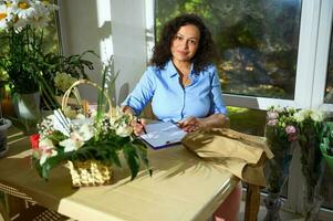 lindo criativo mulher, florista decorador segurando flor arranjo dentro vime cesta, sorridente olhando às Câmera foto