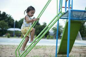 uma menina é escalada acima uma aço escada para uma deslizar dentro uma Parque infantil. foto