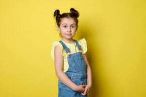 lindo elegante pequeno criança menina com na moda Penteado dentro casual azul jeans, olhando às Câmera. feliz infância. foto