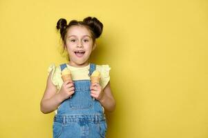 lindo feliz pré-escolar pequeno menina 6 anos velho, sorridente olhando às Câmera, em pé com waffle cones do gelo creme foto