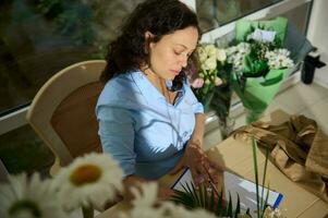 topo Visão étnico mulher com prancheta, trabalhando dentro floral Projeto estúdio. natureza, jardim às lar. arranjos e presentes foto