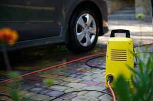 foco em uma brilhante amarelo carro limpeza equipamento perto uma carro. água Alto pressão limpador, máquina de lavar com mangueira e spray varinha foto