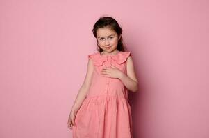 lindo coquete, pequeno criança menina 5-6 anos velho, sorridente olhando às Câmera sobre Rosa isolado fundo foto