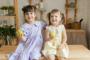 pequeno feliz meninas idiota por aí dentro a cozinha e comer maçãs foto