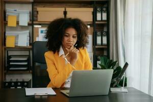 confiante o negócio especialista atraente sorridente jovem mulher digitando computador portátil ang segurando digital tábua em escrivaninha dentro criativo escritório. foto