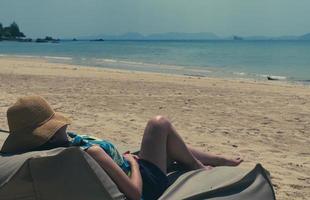 jovem deitada em um saco de feijão na praia para tomar banho de sol nas férias de verão foto