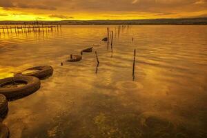 colorida pôr do sol em a lago com pescaria internet dentro água e velho pneus foto