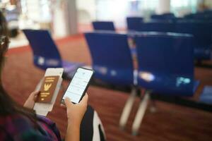 mulher esperando para saída às a aeroporto em seu período de férias aguarde Passaporte e Smartphone enquanto esperando embarque em saída área internacional aeroporto foto