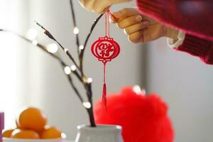 ásia mulher decorado casa para chinês Novo ano celebrações. colocando tradicional pingente para a chinês lunar Novo ano para Boa sorte. chinês palavra significa bênção foto