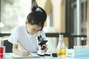 pequeno criança com Aprendendo classe dentro escola laboratório usando microscópio foto