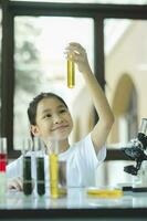 pequeno menina dentro elevação e olhando às substância dentro tubo dentro química Ciência aula. foto