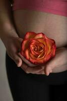 jovem grávida mulher mantém natural rosa Flor fechar para dela barriga. foto