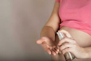 jovem grávida mulher mantém vidro garrafa do corpo óleo fechar para dela barriga. foto