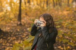 criança menina usando a antiquado Câmera dentro outono natureza. fotógrafo, outono estação e lazer conceito. foto