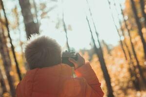 Garoto com retro Câmera levando As fotos ao ar livre dentro outono natureza. lazer e fotógrafos conceito