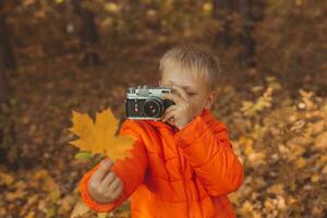 Garoto com retro Câmera levando As fotos ao ar livre dentro outono natureza. lazer e fotógrafos conceito