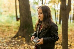 criança menina usando a antiquado Câmera dentro outono natureza. fotógrafo, outono estação e lazer conceito. foto