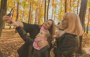 três gerações do mulheres e cachorro sentir Diversão Veja às Câmera posando para auto-retrato cenário junto, engraçado animado criança, mãe e avó ter Diversão apreciar final de semana levar selfie em gadget dentro outono foto