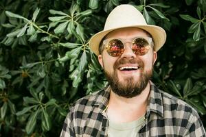 rindo atraente homem vestindo chapéu sobre verde árvore fundo - emoção e período de férias viagem feriados conceito foto