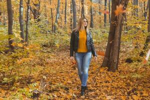 fofa risonho mulher segurando outono folhas e anda em dentro outono parque. sazonal, estilo de vida e lazer conceito. foto