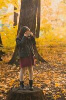 criança menina usando a antiquado Câmera dentro outono natureza. fotógrafo, outono estação e lazer conceito. foto