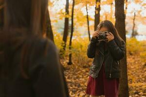 criança levando cenário dela mãe em retro Câmera dentro outono parque. hobbies e lazer conceito. foto