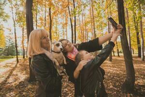 mãe, avó e pequeno neta com jack russell terrier cachorro levando selfie de Smartphone ao ar livre dentro outono natureza. família, animais de estimação e geração conceito foto