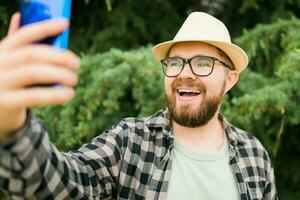 homem levando selfie retrato sobre árvore fundo - feliz milenar cara desfrutando verão feriados dentro cidade - juventude e tecnologias foto