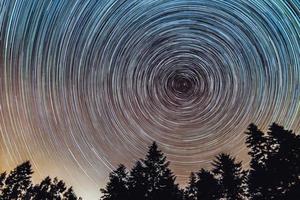 trilhas de estrelas no céu noturno, lapso de tempo da trilha de estrelas, pinheiros em primeiro plano, avala, belgrado, sérvia. o céu noturno é astronomicamente preciso. foto