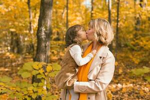 mulher com criança menina ao ar livre dentro cair. criança se beijando mãe. mães dia feriado e outono conceito. foto