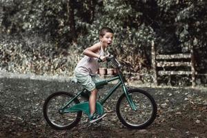 um menino com cara engraçada andando em sua velha bicicleta rústica. um menino anda de bicicleta velha no quintal e faz uma careta. foto