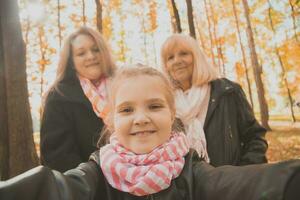 três gerações do mulheres e cachorro sentir Diversão Veja às Câmera posando para auto-retrato cenário junto, engraçado animado criança, mãe e avó ter Diversão apreciar final de semana levar selfie em gadget dentro outono foto