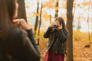 criança menina fotógrafo leva As fotos do uma mãe dentro a parque dentro outono. hobbies, foto arte e lazer conceito.