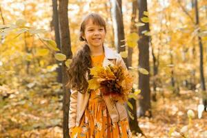 pequeno criança menina com outono laranja folhas dentro uma parque. estilo de vida, outono estação e crianças conceito. foto