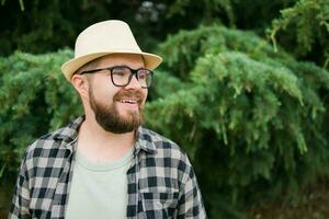 rindo atraente homem vestindo chapéu sobre verde árvore fundo com cópia de espaço e esvaziar espaço para publicidade - emoção e período de férias viagem feriados conceito foto