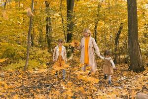 mãe e pequeno filhas desfrutando agradável outono dia dentro uma parque. temporada, família e crianças conceito. foto
