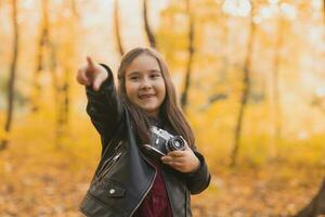 criança menina usando a antiquado Câmera dentro outono natureza. fotógrafo, outono estação e lazer conceito. foto